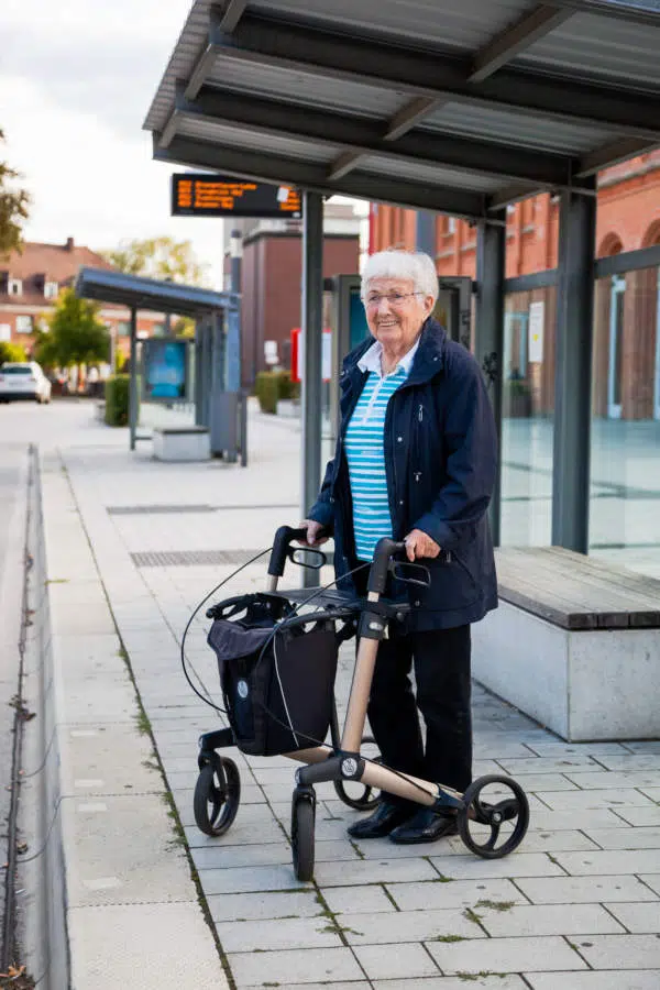 Seniorin mit Rollator an Bushaltestelle