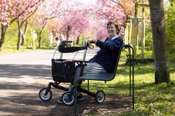 Seniorin sitzt im Park mit Rollator neben sich